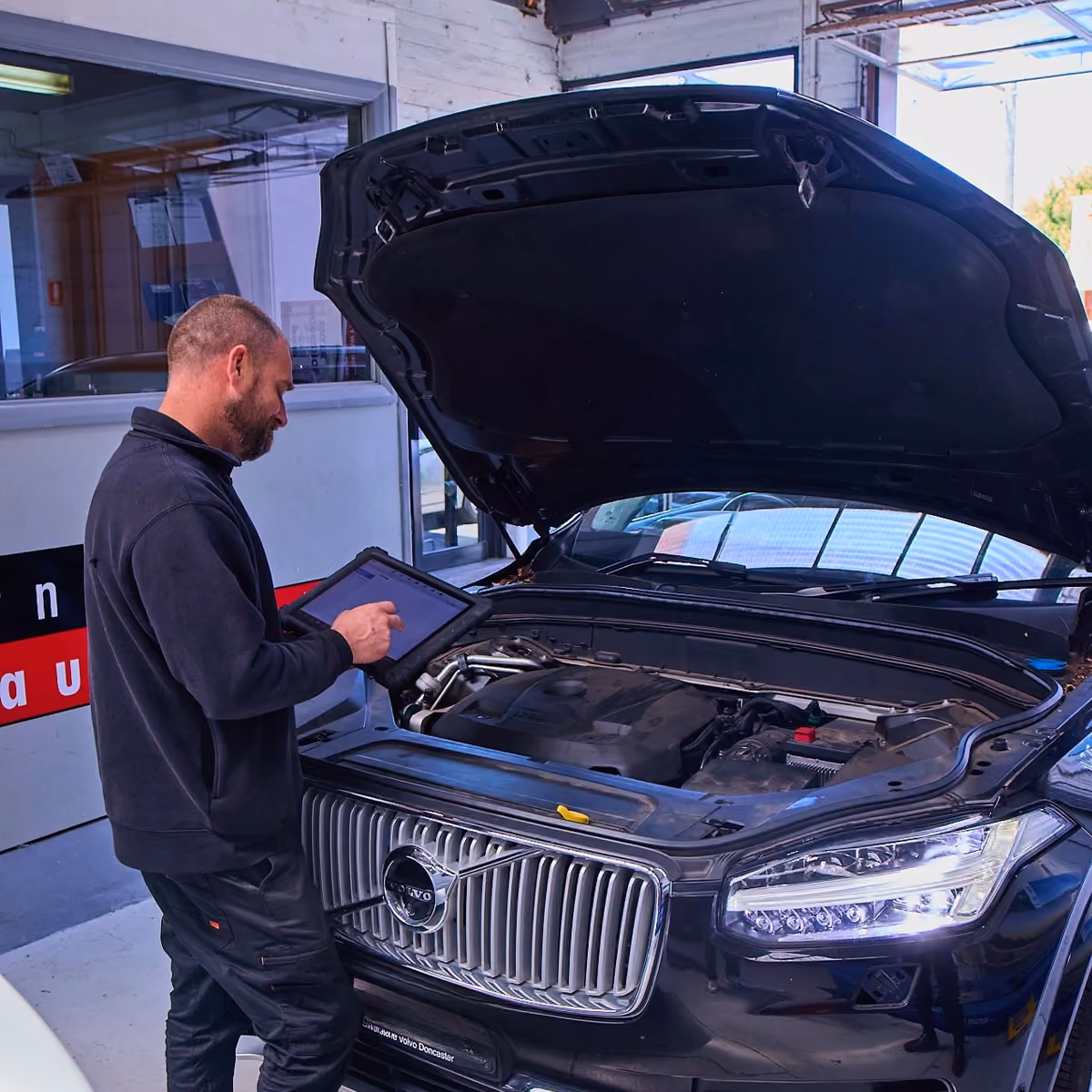 Technician using tablet to run EFI diagnostics on Volvo engine.
