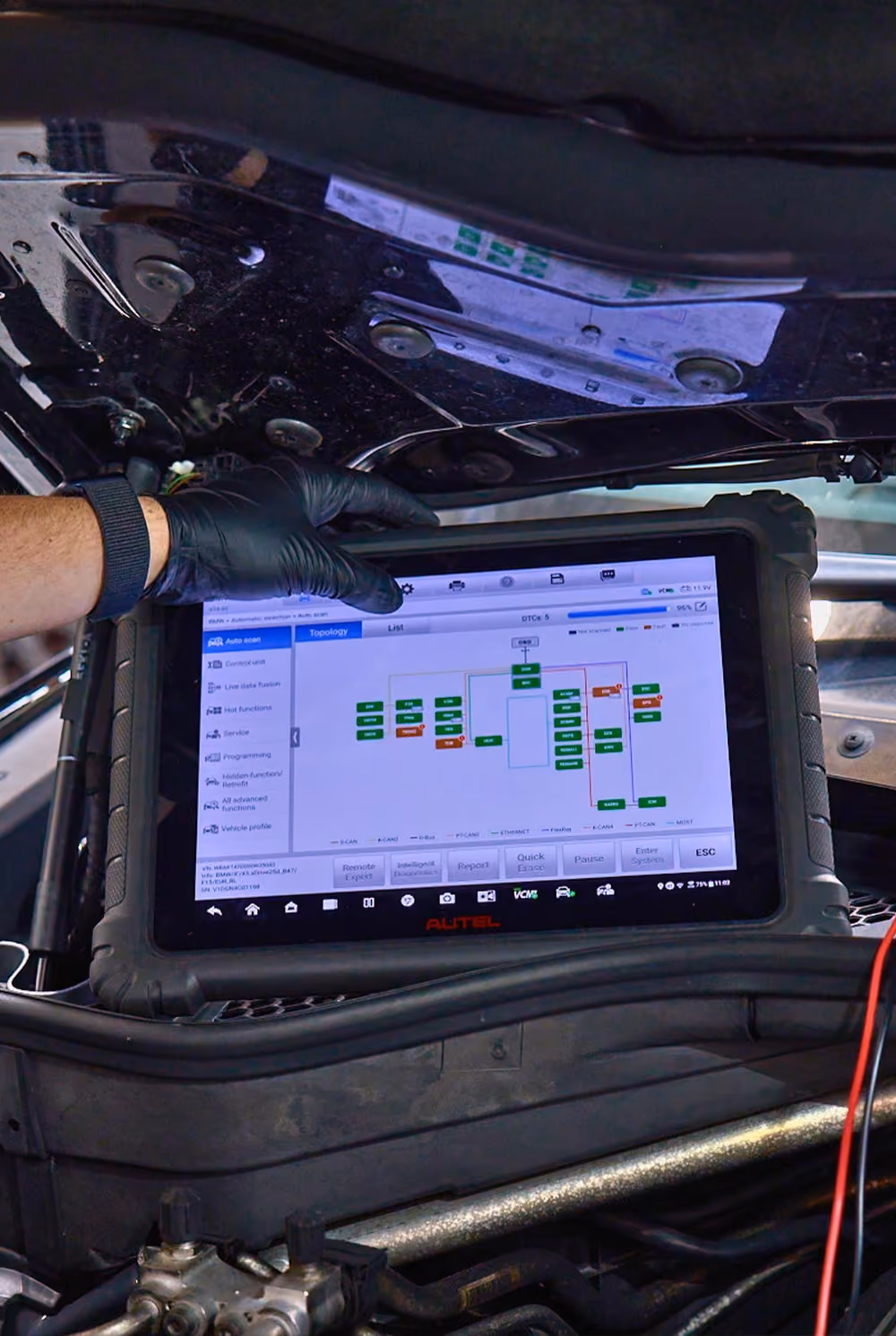 Mechanic using diagnostic tool under car bonnet.