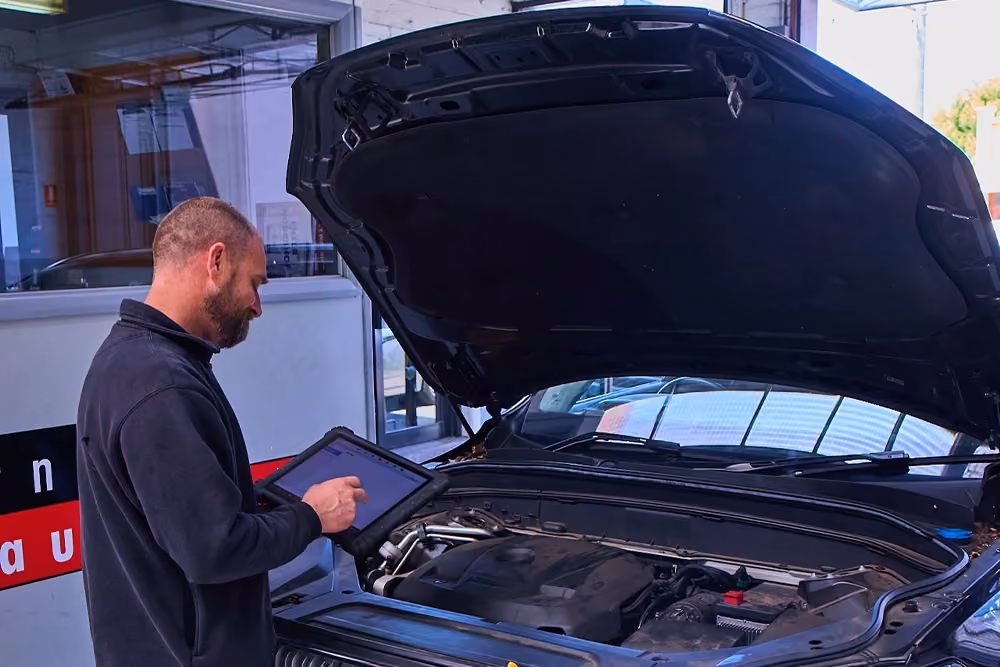 Technician performing vehicle diagnostics using a tablet during an automotive inspection.