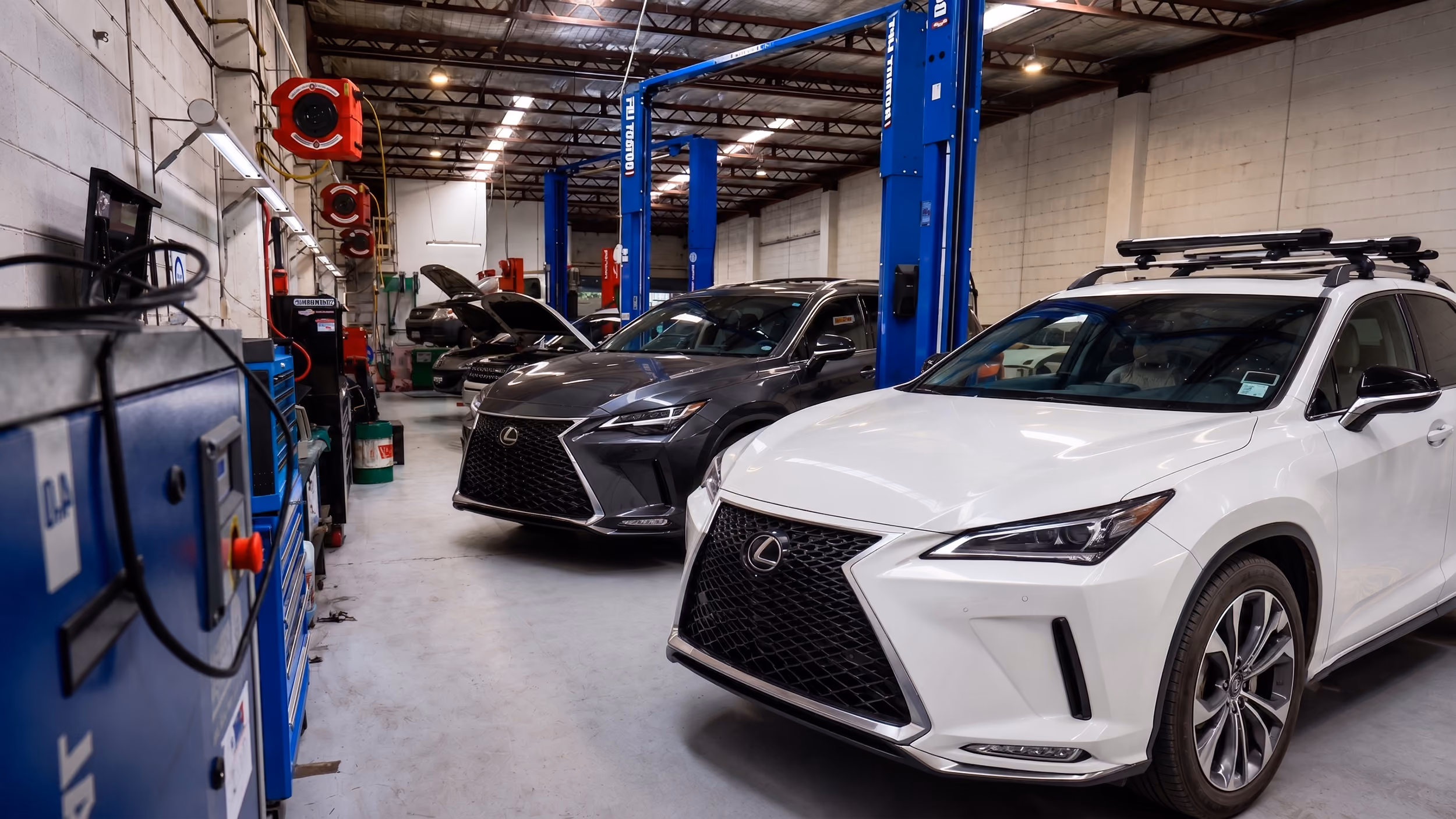 Modern automotive workshop with a black Lexus SUV parked inside a service bay and additional Lexus vehicles visible outside the open roller door.