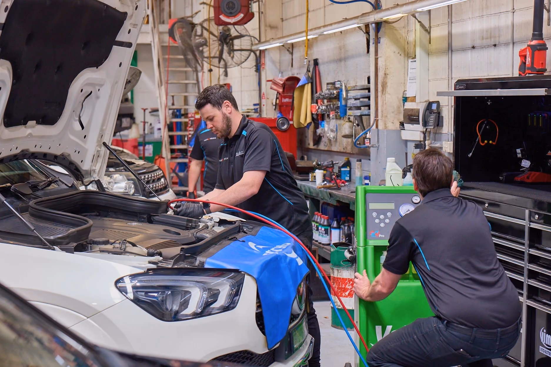 Automotive technicians carrying out vehicle diagnostics and servicing in a workshop.