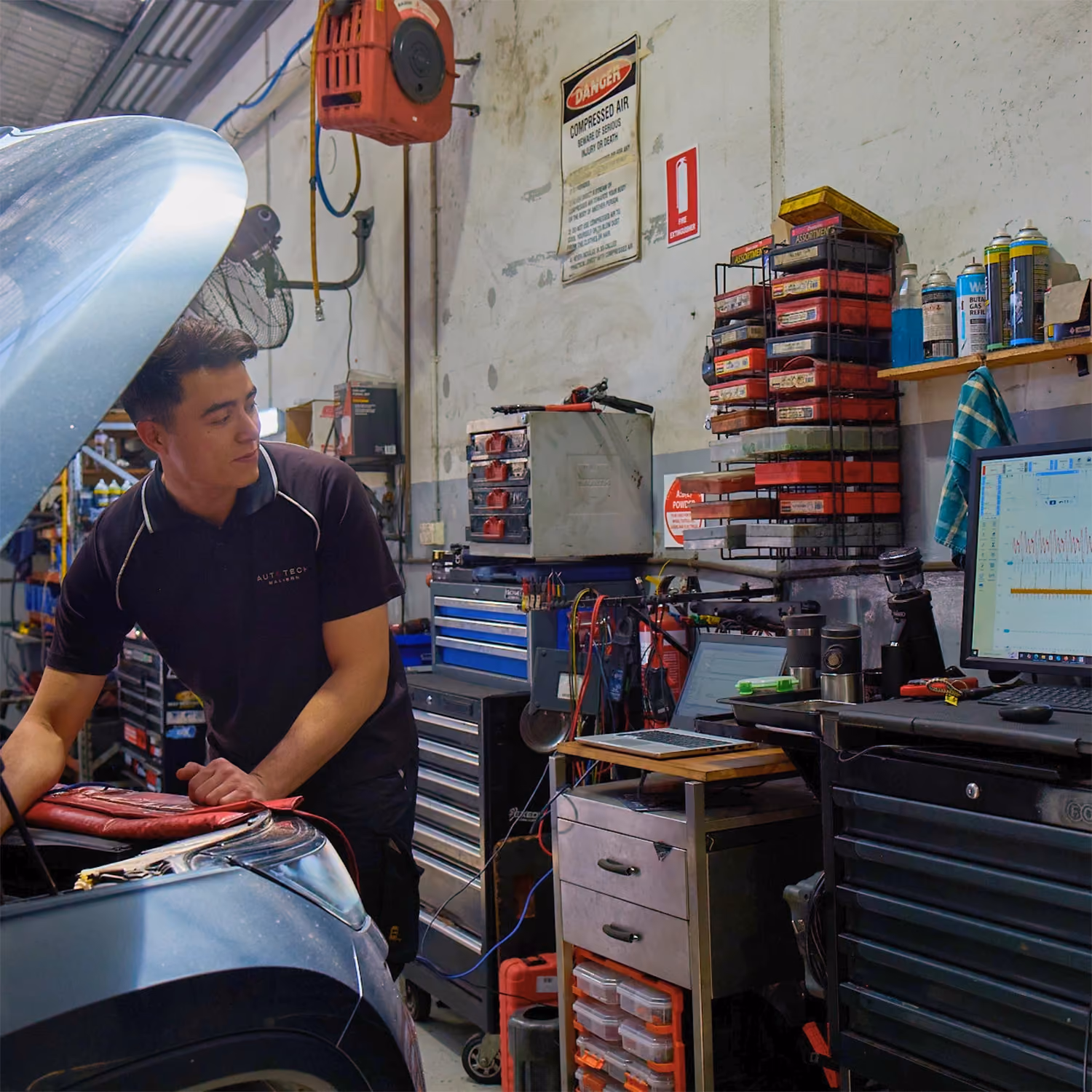 Automotive technician inspecting Lexus vehicles in a workshop with multiple cars undergoing servicing.