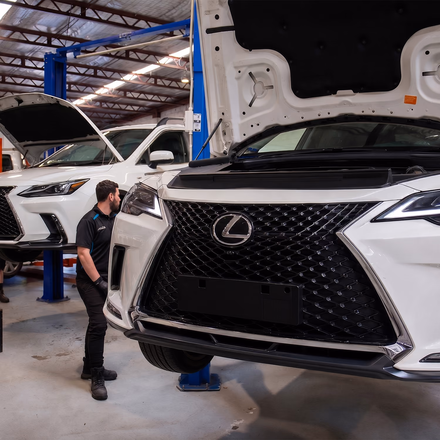 Automotive technicians servicing a white Lexus vehicle in a professional workshop equipped with diagnostic and repair equipment.