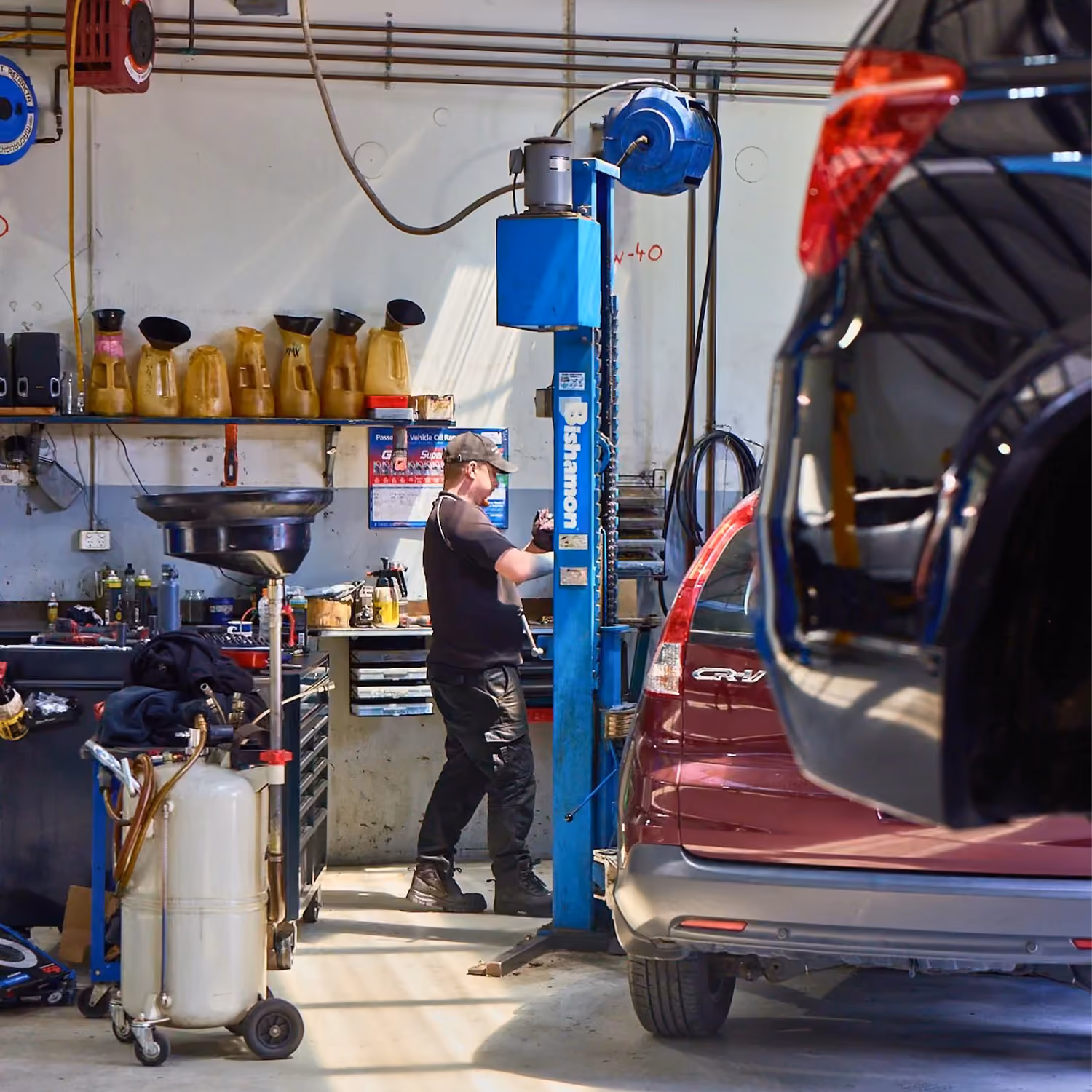Technician working on vehicle near hoist in mechanical workshop.