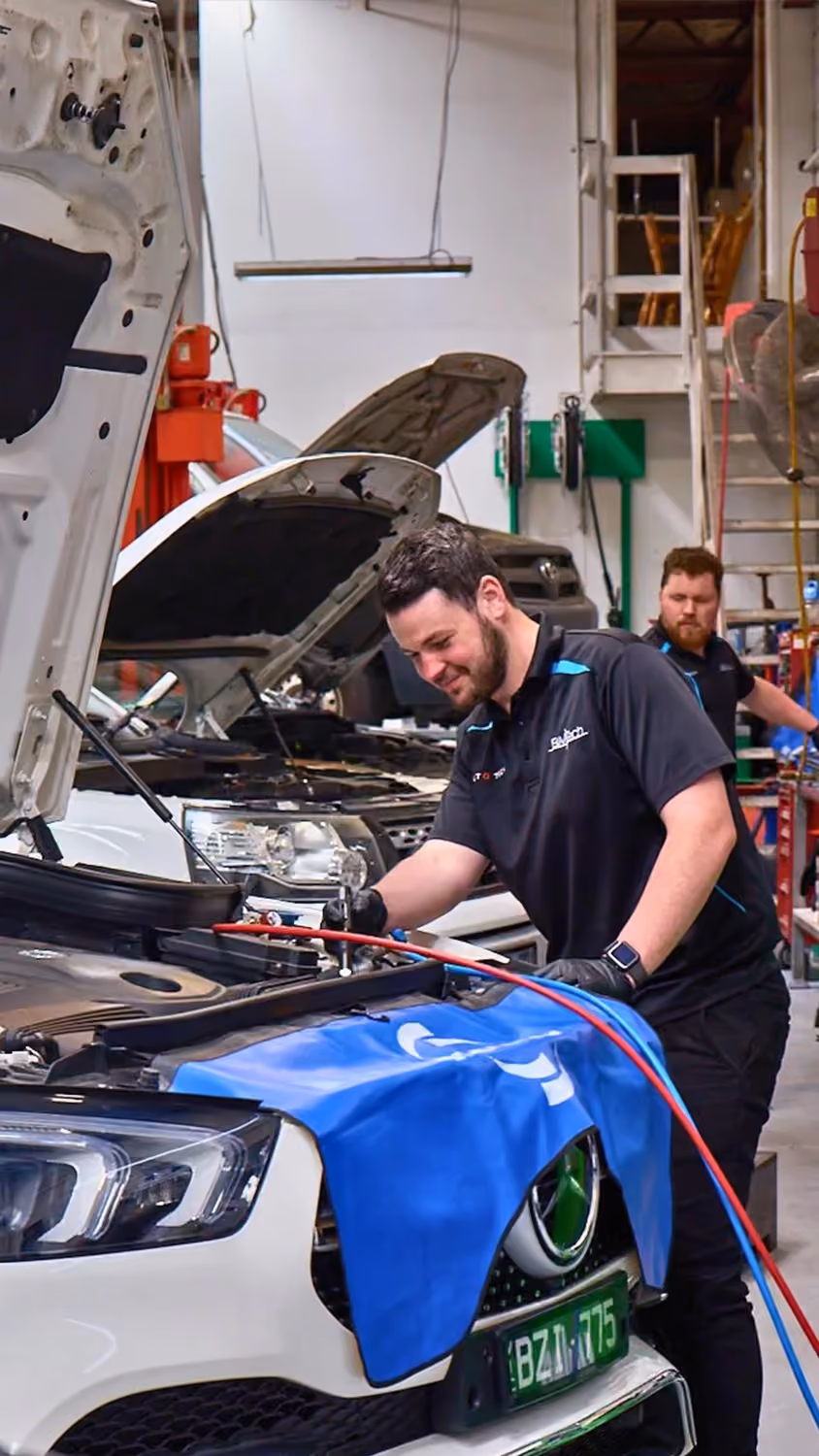 Technician performing repair service on a Mercedes in a workshop.