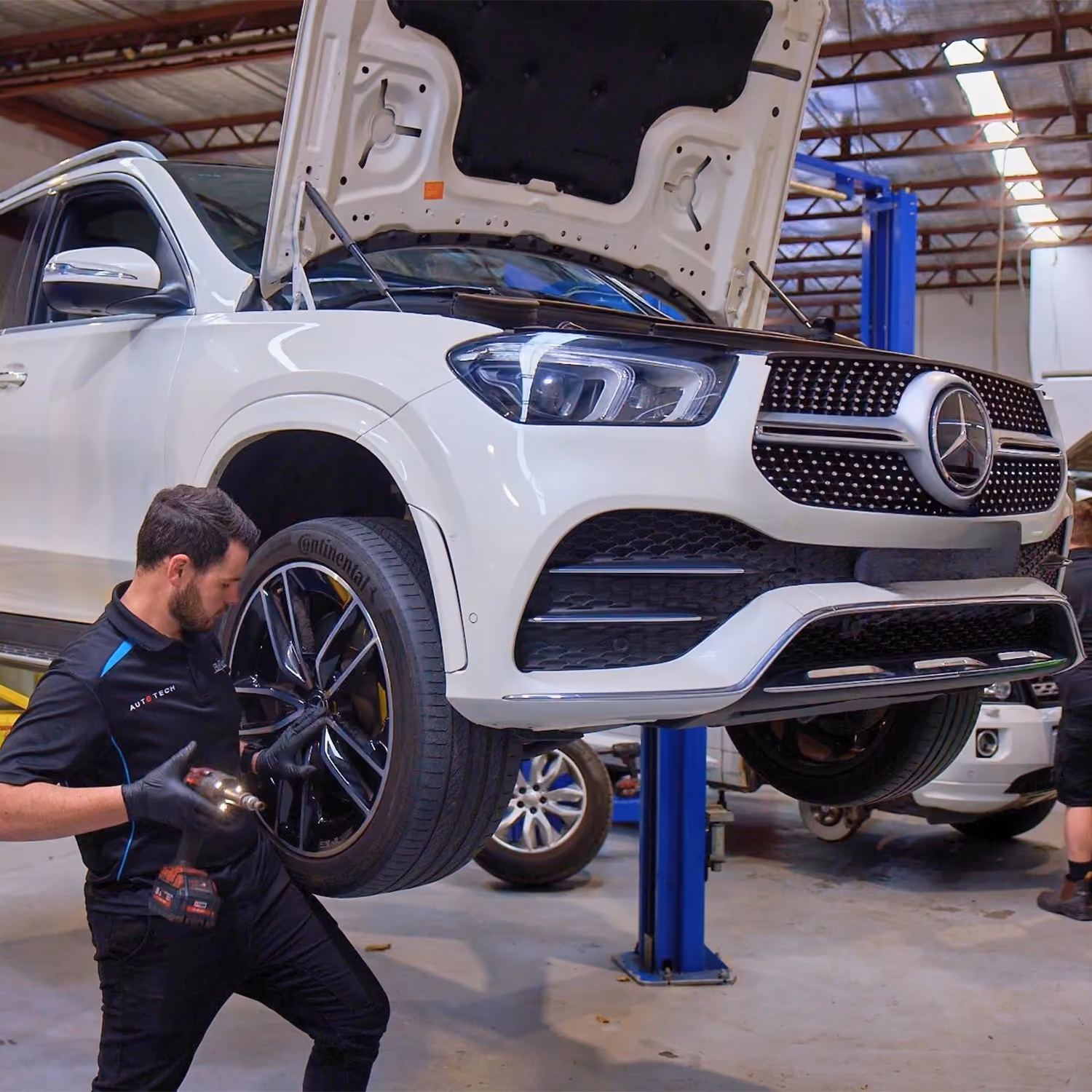 Mechanic servicing wheel and brakes on Mercedes SUV in workshop.