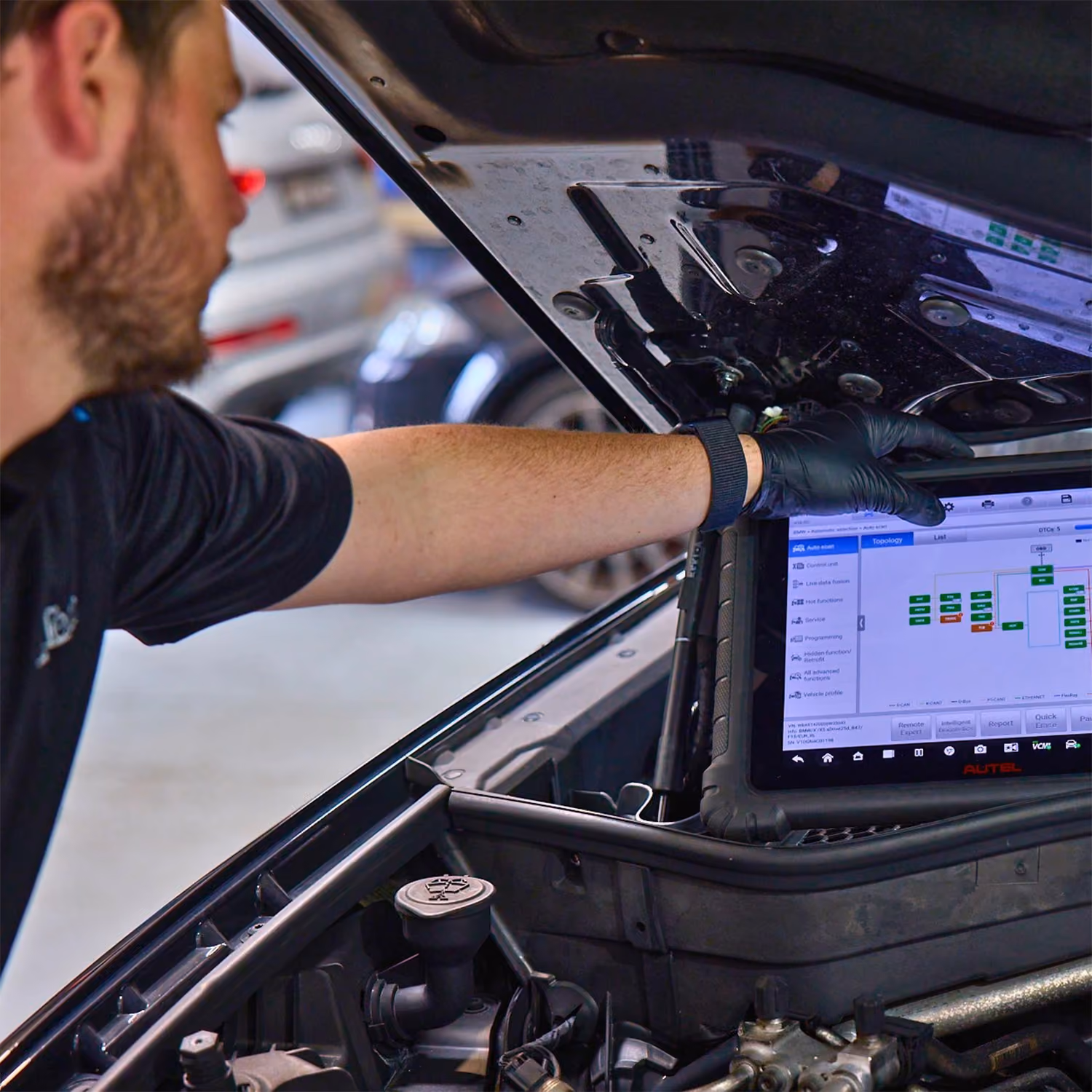 Technician performing vehicle diagnostics using a scan tool connected to the engine bay during an automotive inspection.