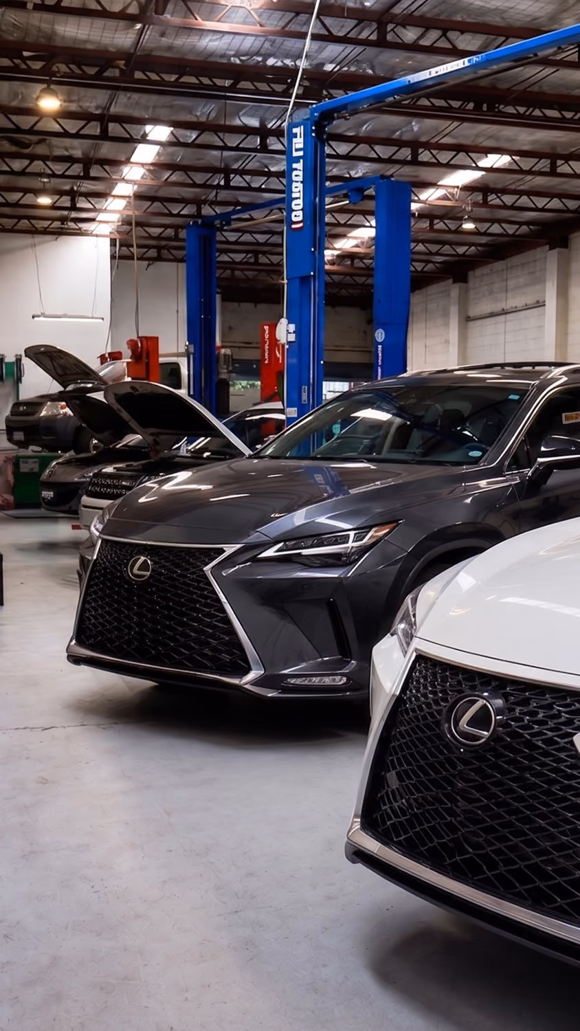 Modern automotive workshop with a black Lexus SUV parked inside a service bay and additional Lexus vehicles visible outside the open roller door.