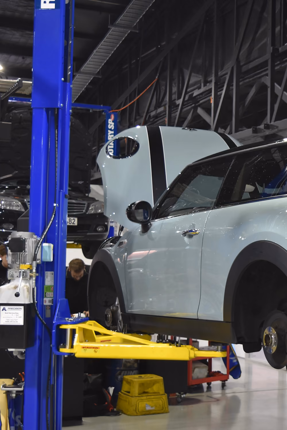 Mechanic removing wheel from white Mercedes SUV on hoist.