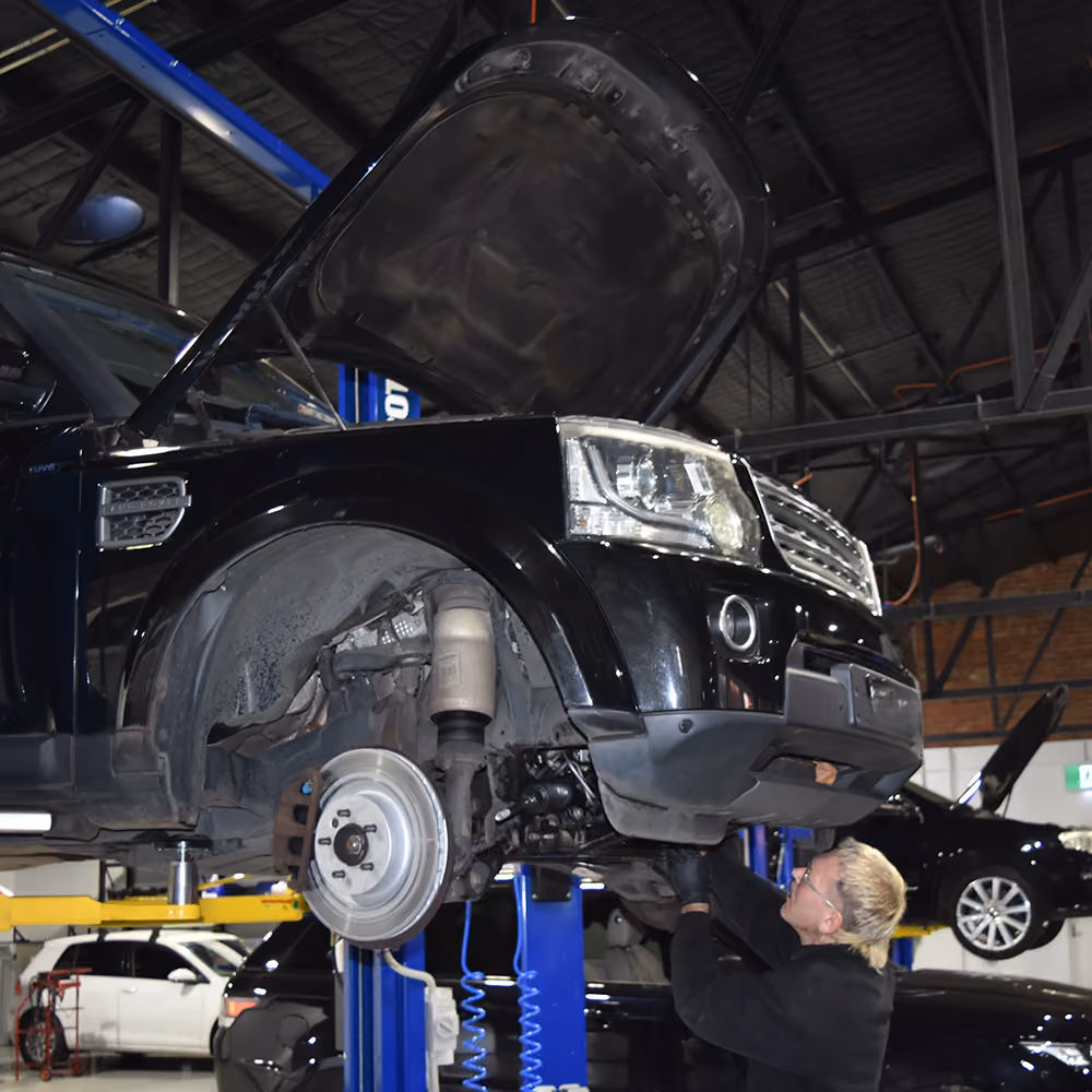 Technician replacing brake components on a raised Range Rover.