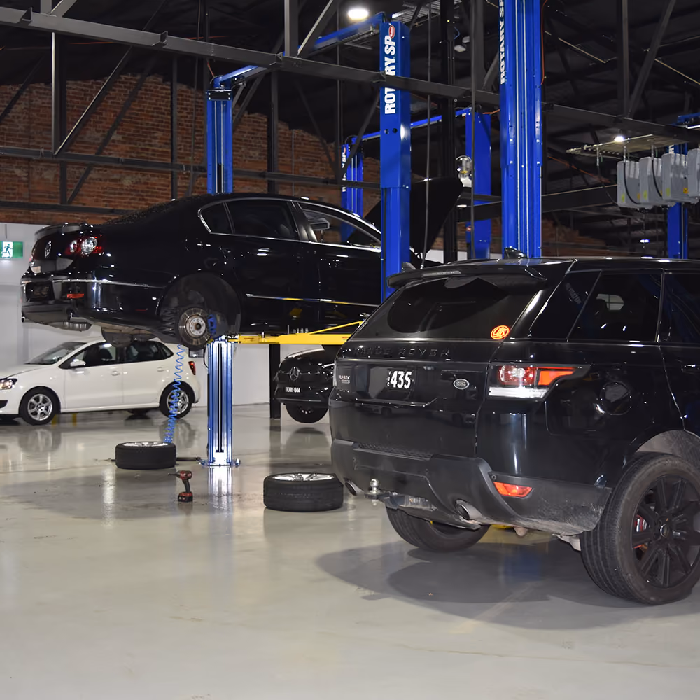 Automotive workshop with multiple vehicles on hoists undergoing servicing and repairs.