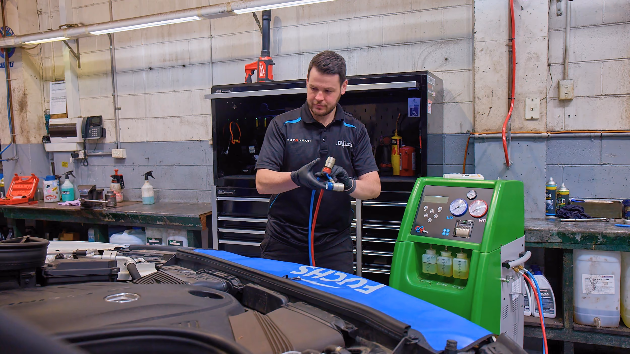 Auto technician servicing car air conditioning system and checking refrigerant levels.
