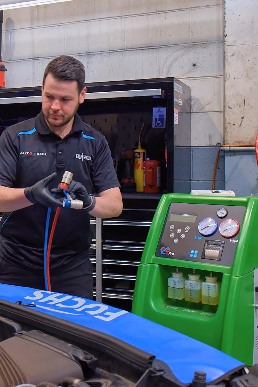 Auto technician servicing car air conditioning system and checking refrigerant levels.