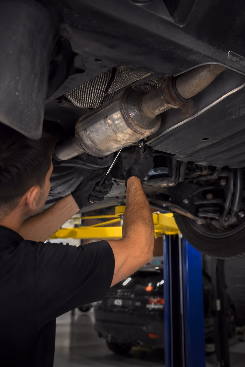 Technician inspecting and repairing a vehicle's exhaust system while working underneath a car on a hoist