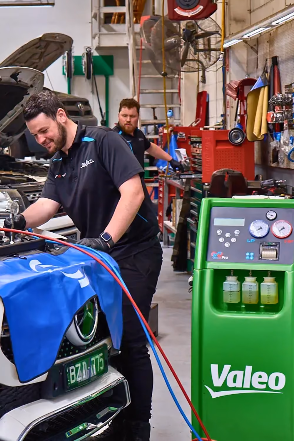 Technician performing vehicle air conditioning servicing using an A/C refrigerant recovery and recharge machine.