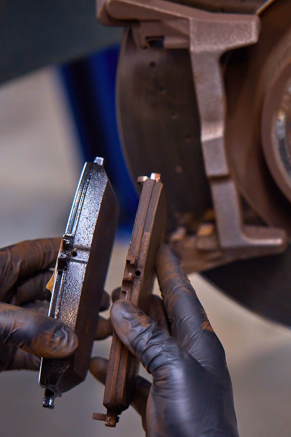 Technician comparing new and worn brake pads during a vehicle brake service.