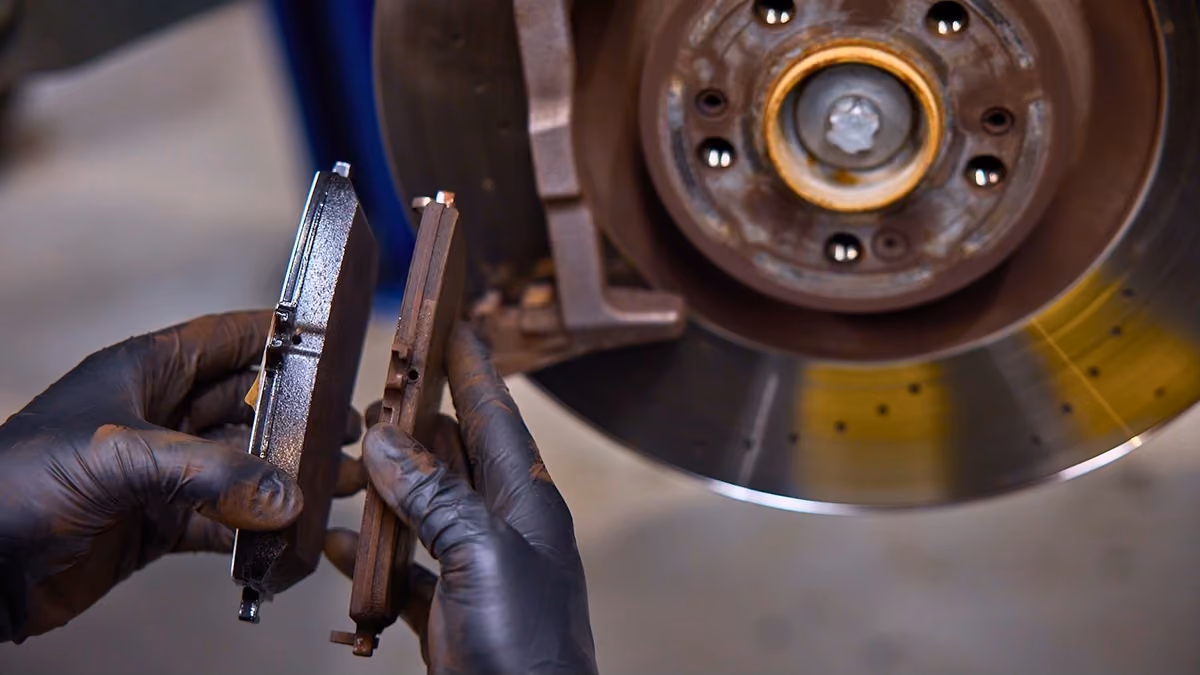 Technician comparing worn and new brake pads during a Range Rover brake inspection.