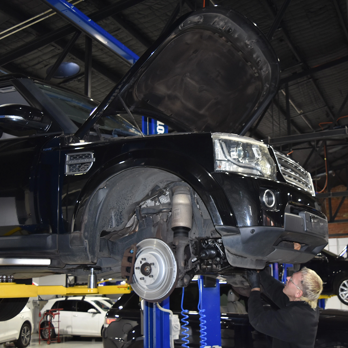 Auto Tech technician working beneath a black Land Rover raised on a workshop hoist.