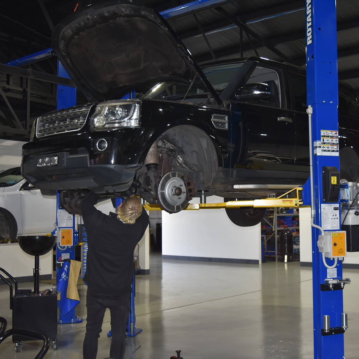 Auto Tech technician servicing a black Land Rover raised on a workshop hoist.