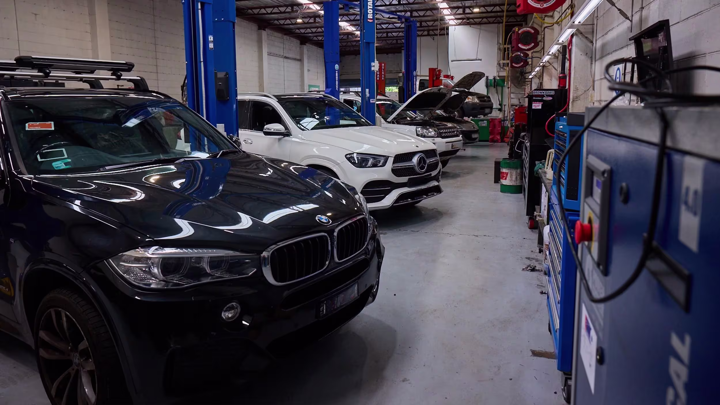 Black BMW and white Mercedes vehicles lined up inside Auto Tech workshop with car lifts in Melbourne.