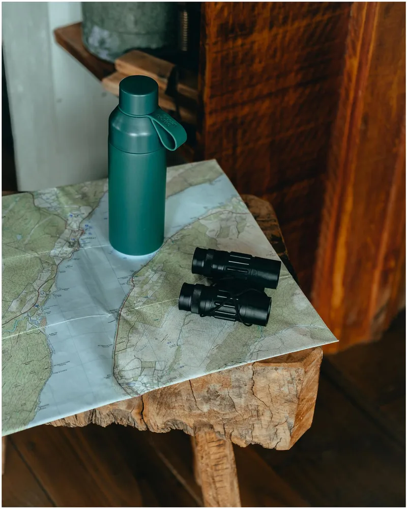 Branded green water bottle styled with binoculars and a map, an example of Maisonette merch