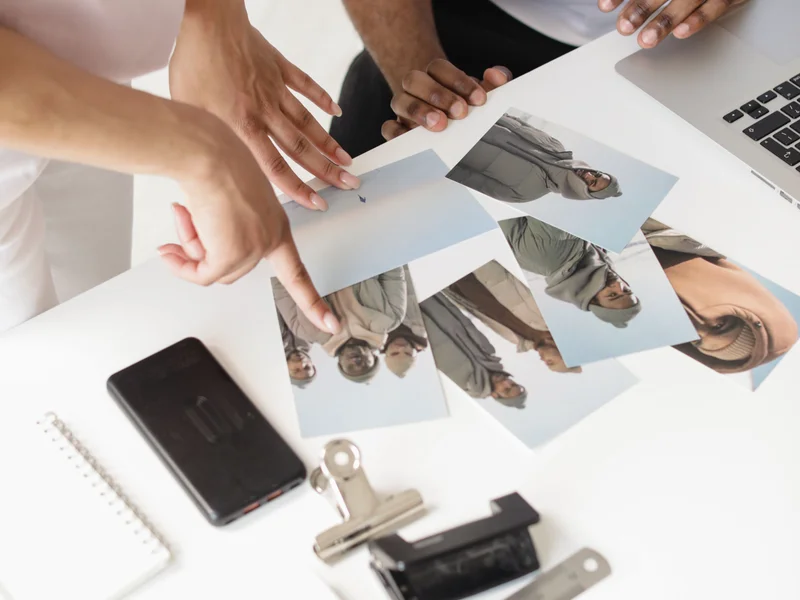 Two people reviewing printed reference photos on a desk with drafting tools