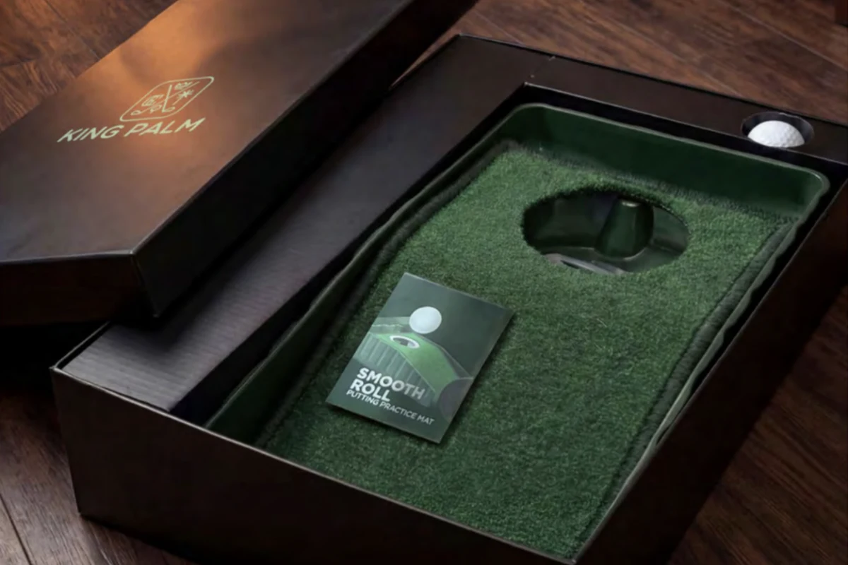 An open branded gift box revealing a custom putting mat, the unboxing moment of a delivered merch drop