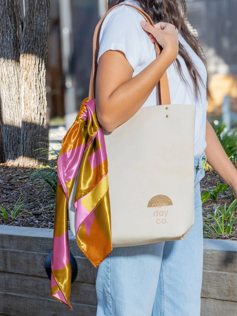 Woman carrying a branded canvas tote bag with a silk scarf tied to the handle, a conference swag drop in motion