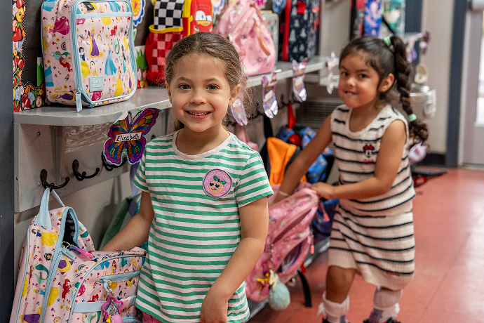 Two young students smiling by school backpack cubbies on arrival day