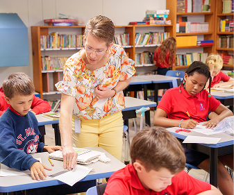 Teacher helping elementary students with classwork in library classroom