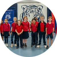 Seven students in red uniforms standing before tiger mascot mural