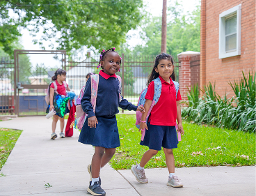 Two smiling students in uniforms walking together outside school