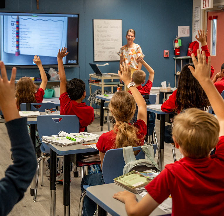 Students in red uniforms raising hands during classroom lesson with teacher
