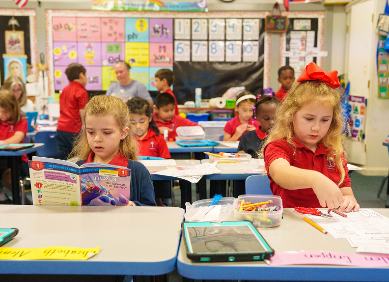 Elementary students in uniform reading and working at classroom desks
