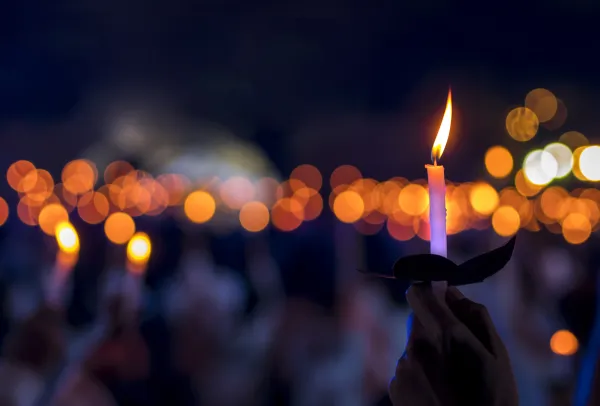 Hand holding a lit candle at an outdoor candlelight gathering