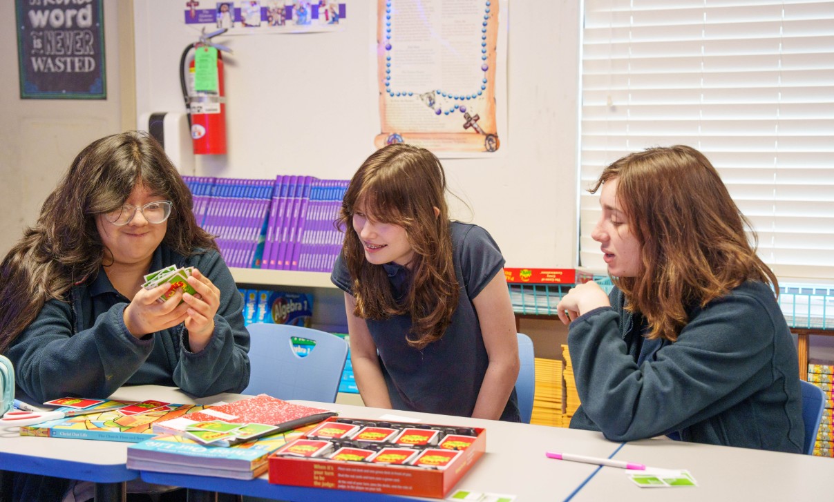 Three students playing a card game together in a classroom