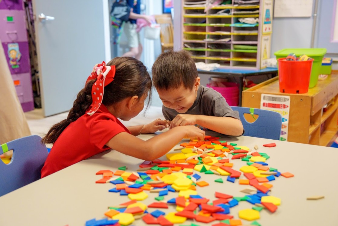 Two students collaborate with colorful pattern blocks at classroom table