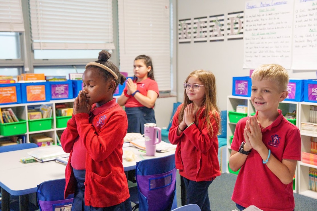 Students in uniform praying together in a Catholic school classroom