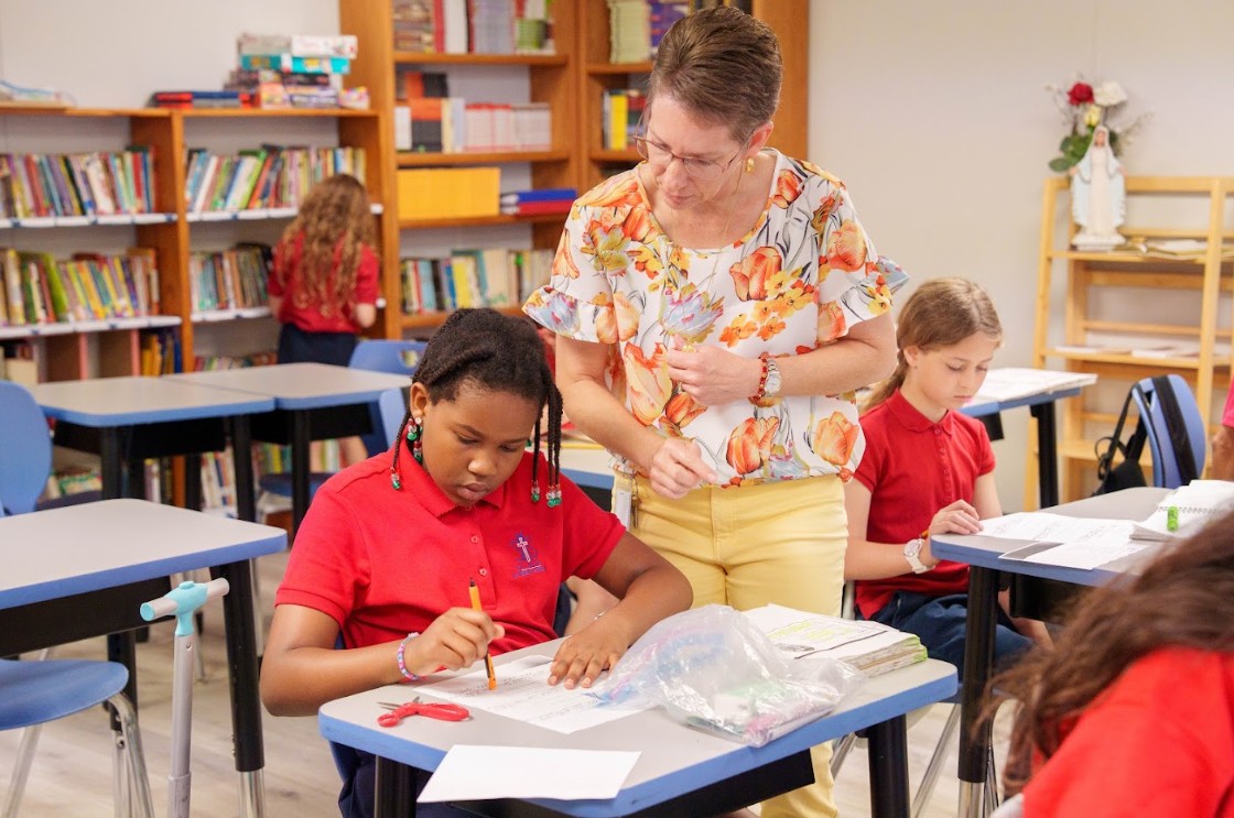 Teacher helping a student with a writing assignment at her desk