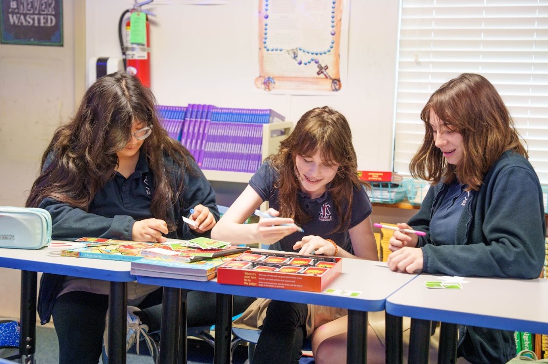 Three students playing a board game together at classroom desks