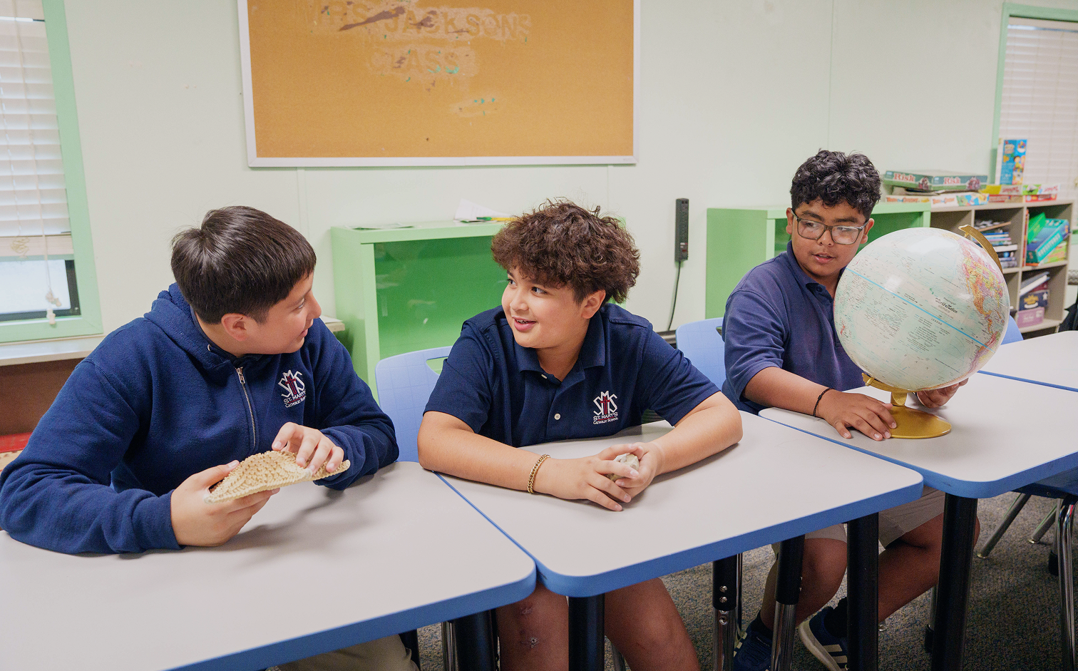 Three middle school students examining a globe and fossil in classroom