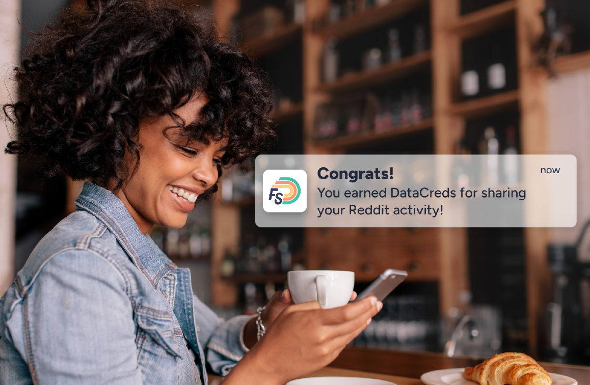 Woman smiling at her phone, with a notification showing she's earned DataCreds for sharing her activity