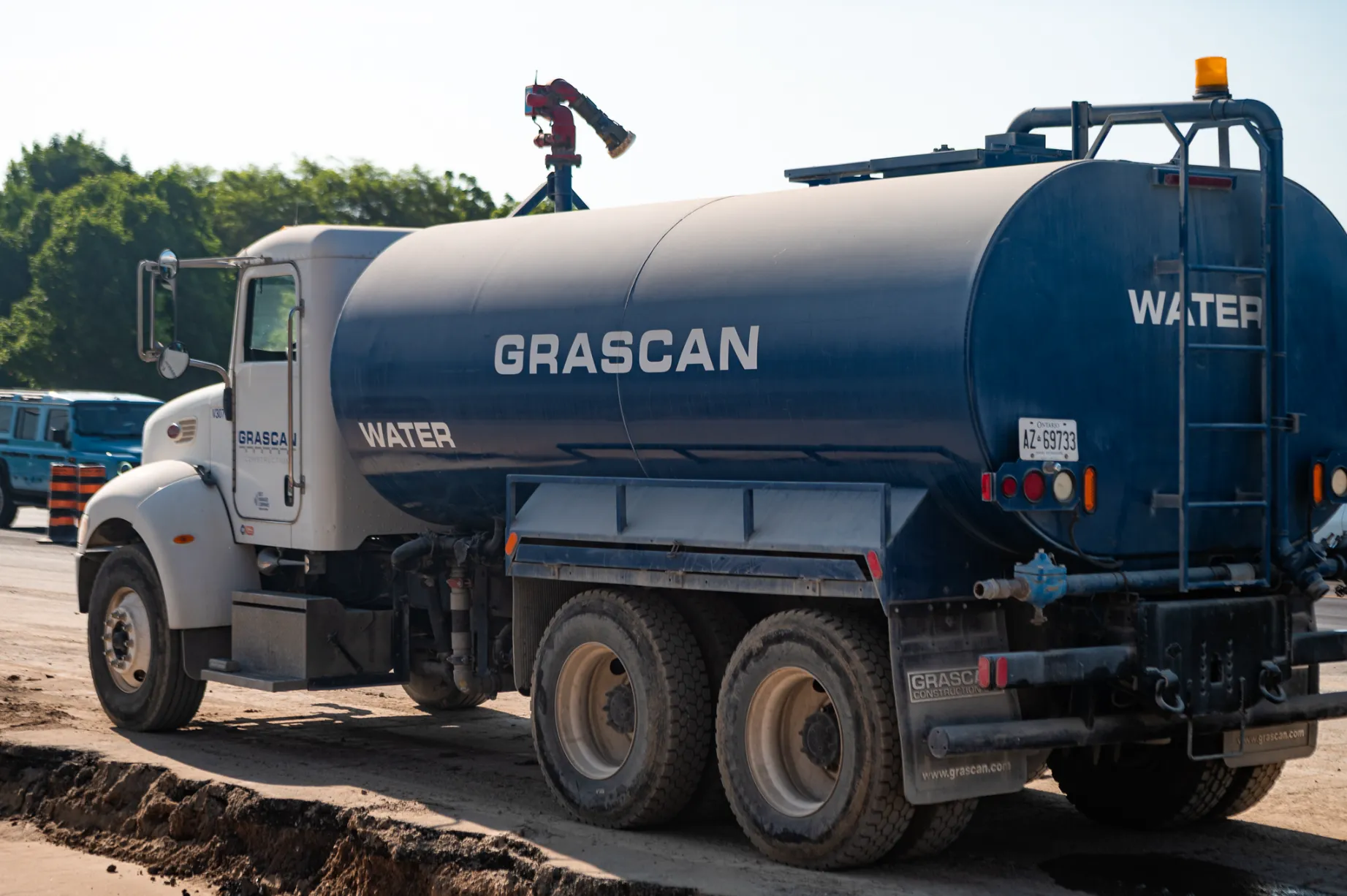 Blue GRASCAN water tanker truck parked on a dirt road with trees in the background.