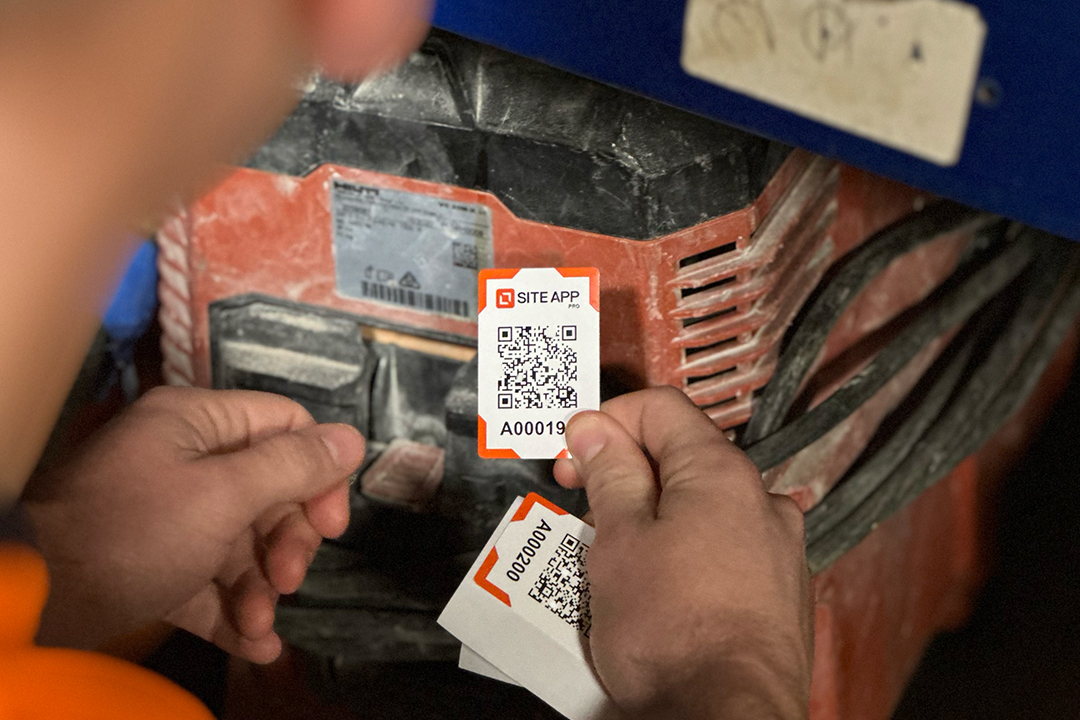 Person holding Site App Pro QR code check-in tags near a piece of industrial equipment.