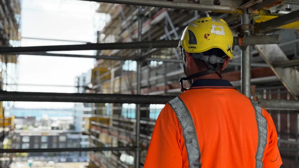 Worker in hard hat and hi-vis seen from behind on a scaffolded building