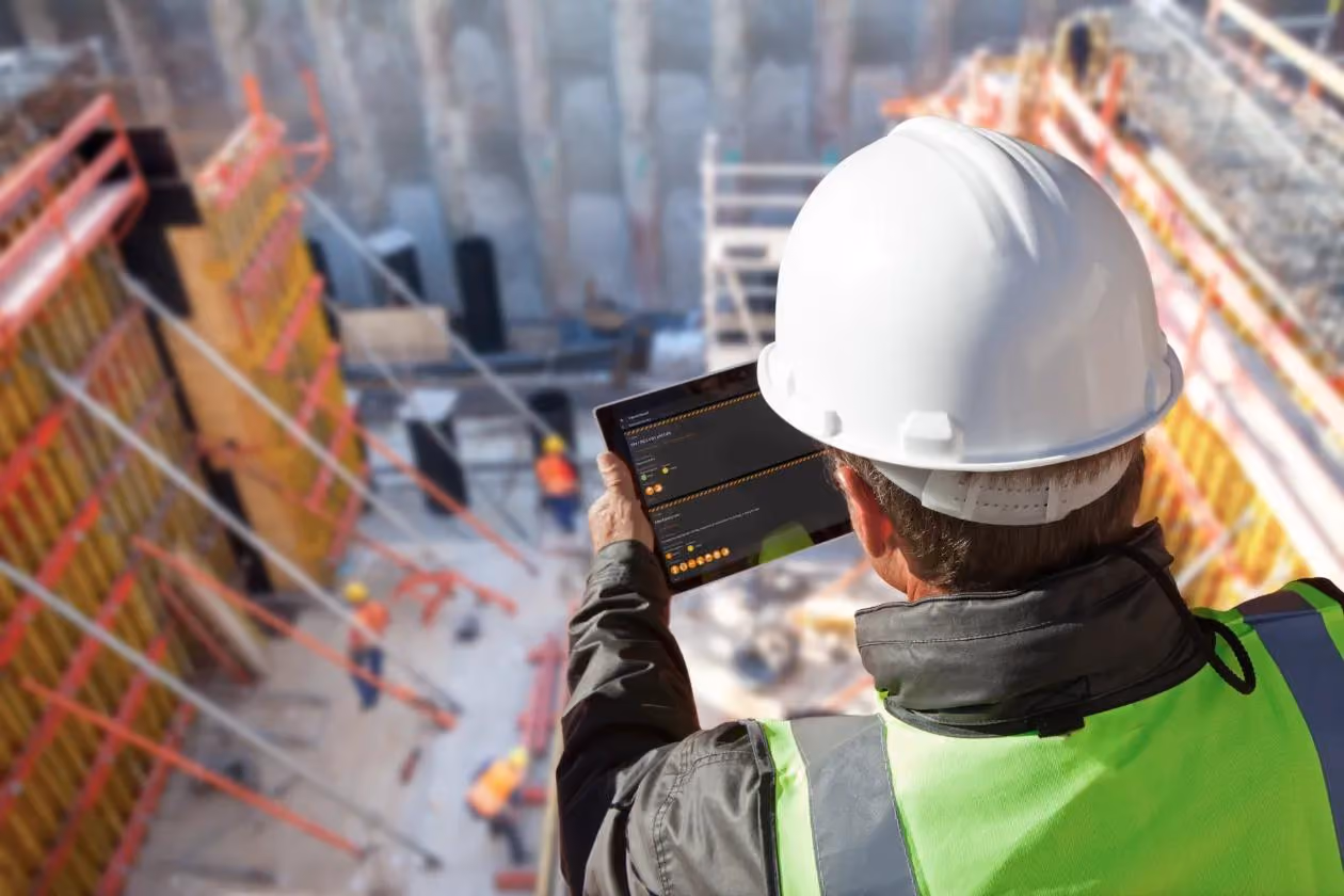 Site supervisor in a hard hat using a tablet above a busy construction site