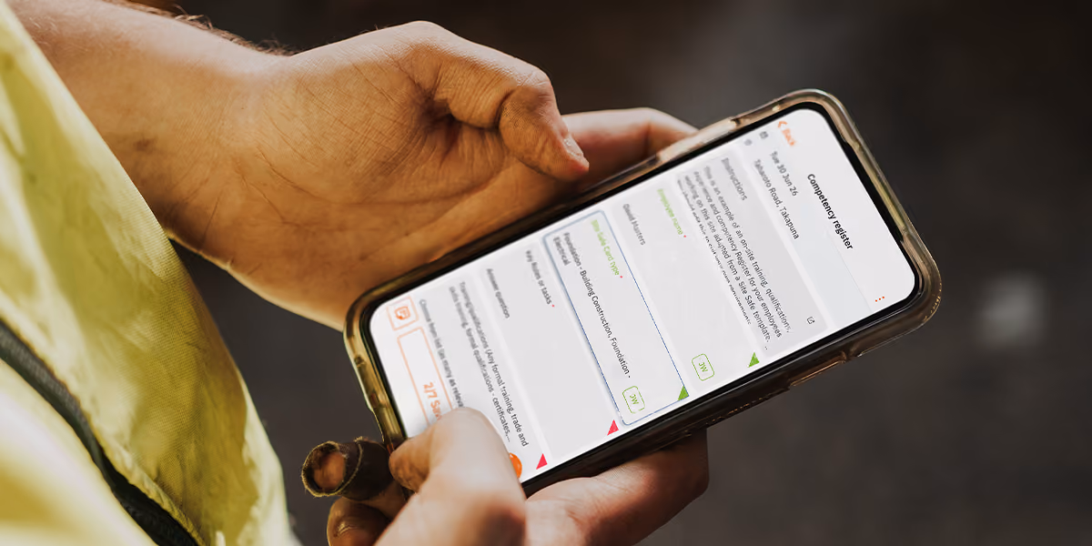 Worker in a hi-vis jacket holding a phone showing a safety checklist form on site