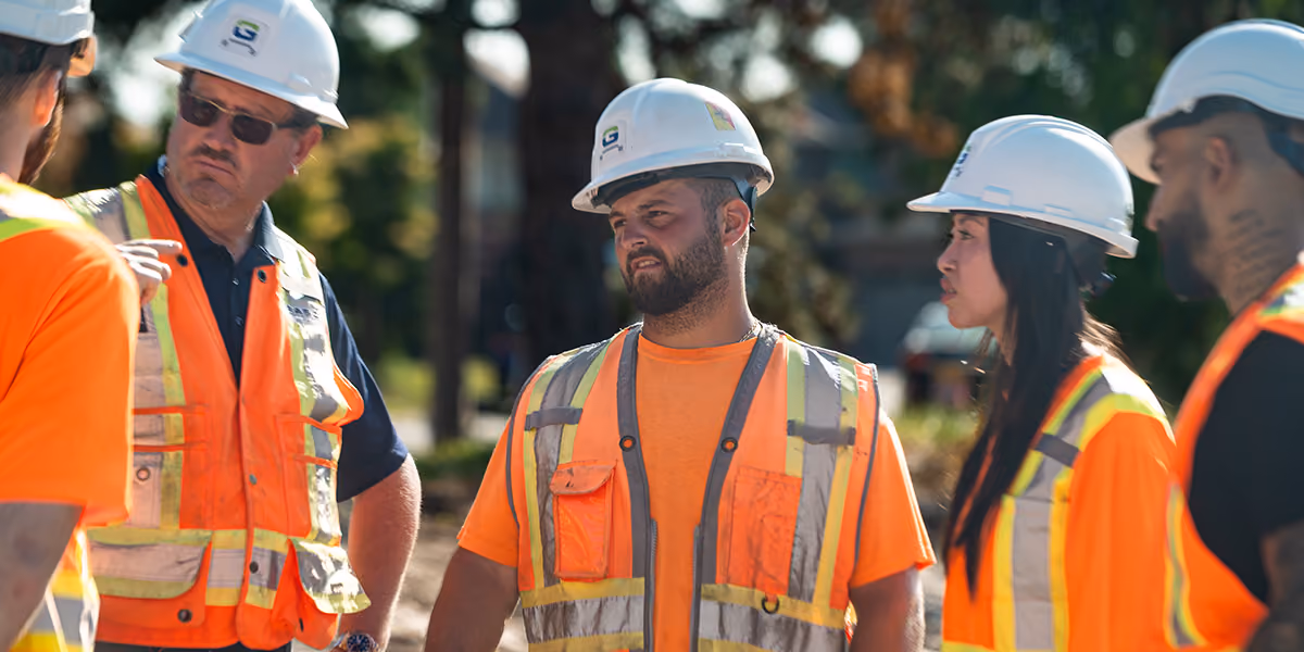 Construction crew in hard hats and hi-vis vests gathered outdoors for a toolbox talk