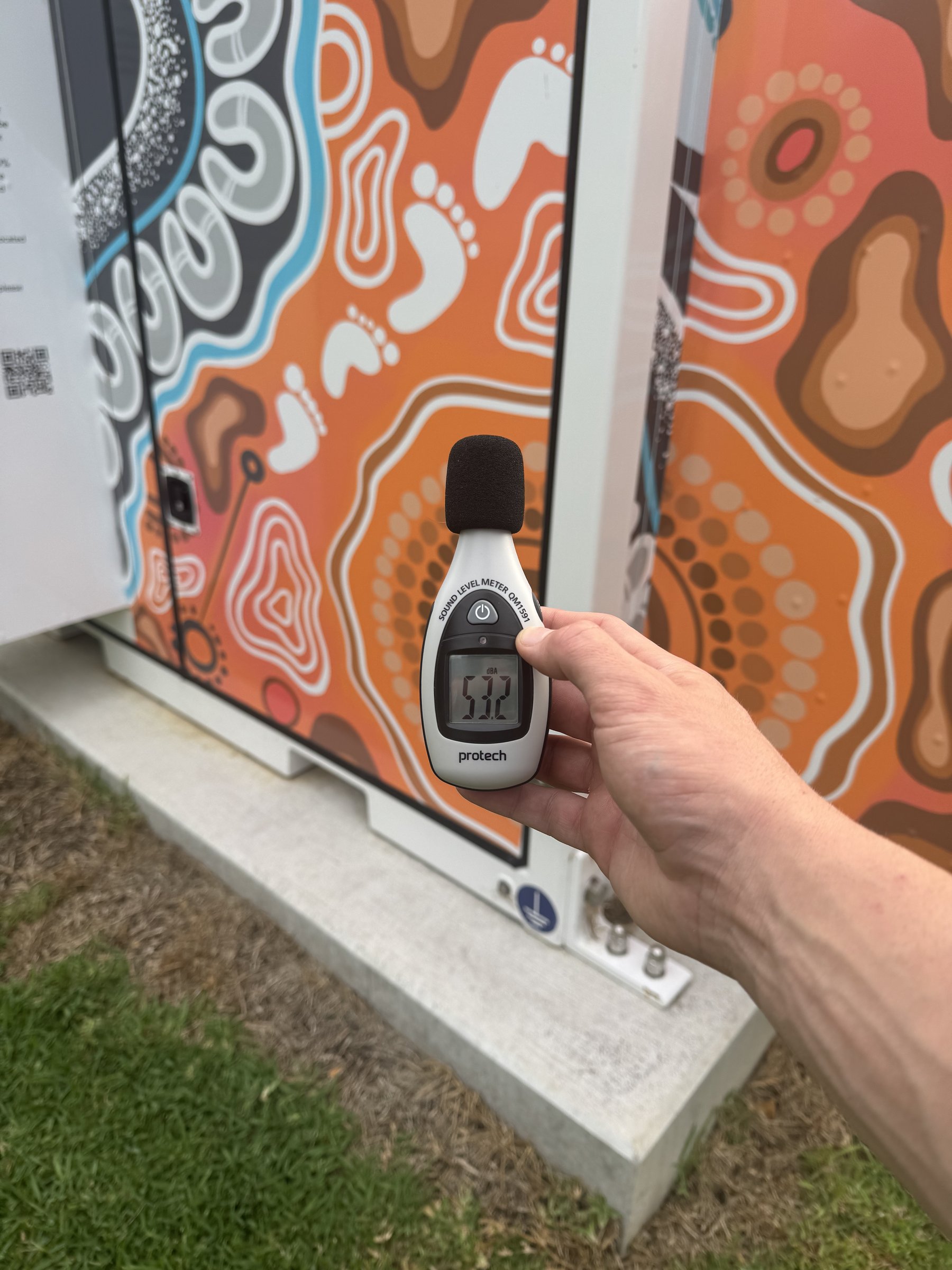 Hand-held sound level meter reading 53.2 dBA beside a battery storage cabinet