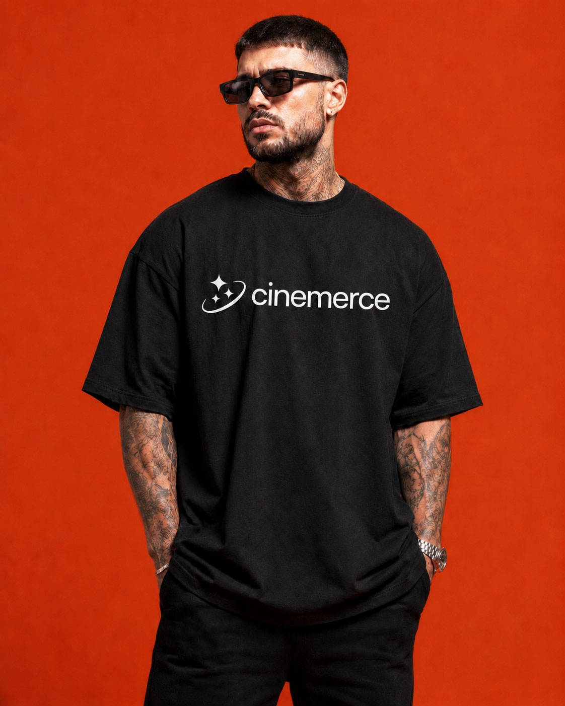 Man with tattoos and sunglasses wearing black Cinemerce t-shirt against red background.